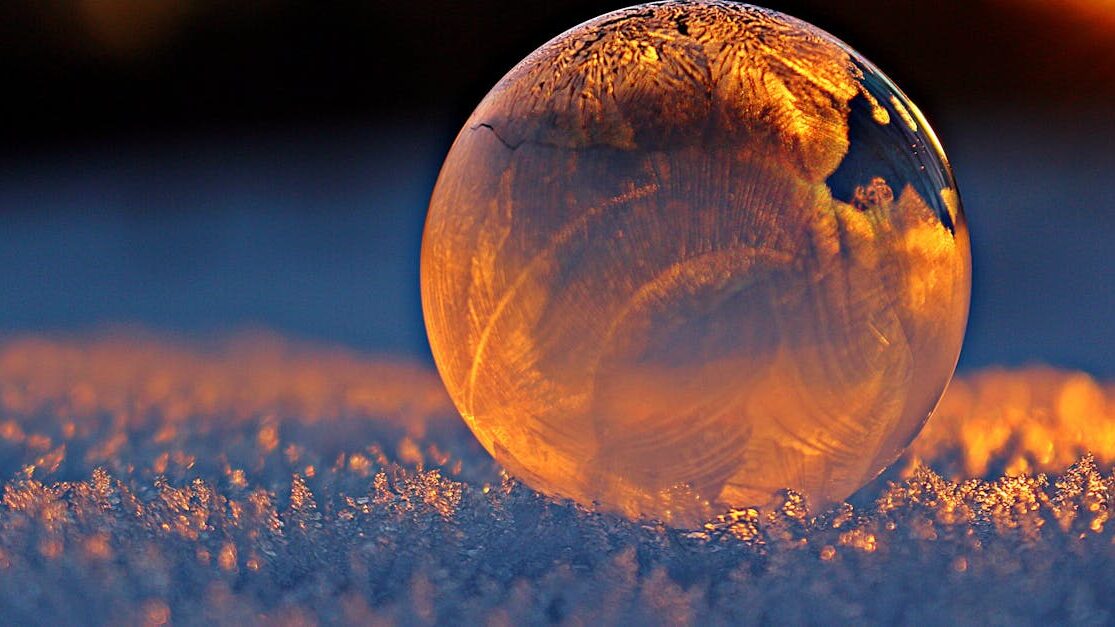 Close-up shot of a frozen bubble with warm reflections resting on a snowy surface at twilight.