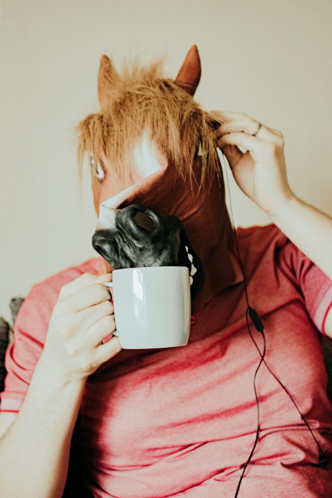 A humorous image of a normal person wearing a horse mask while drinking from a mug indoors.